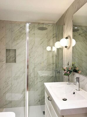 Ein modernes Badezimmer mit einer gläsernen Dusche, einem weißen Waschbecken und einem Spiegel mit Wandleuchten.