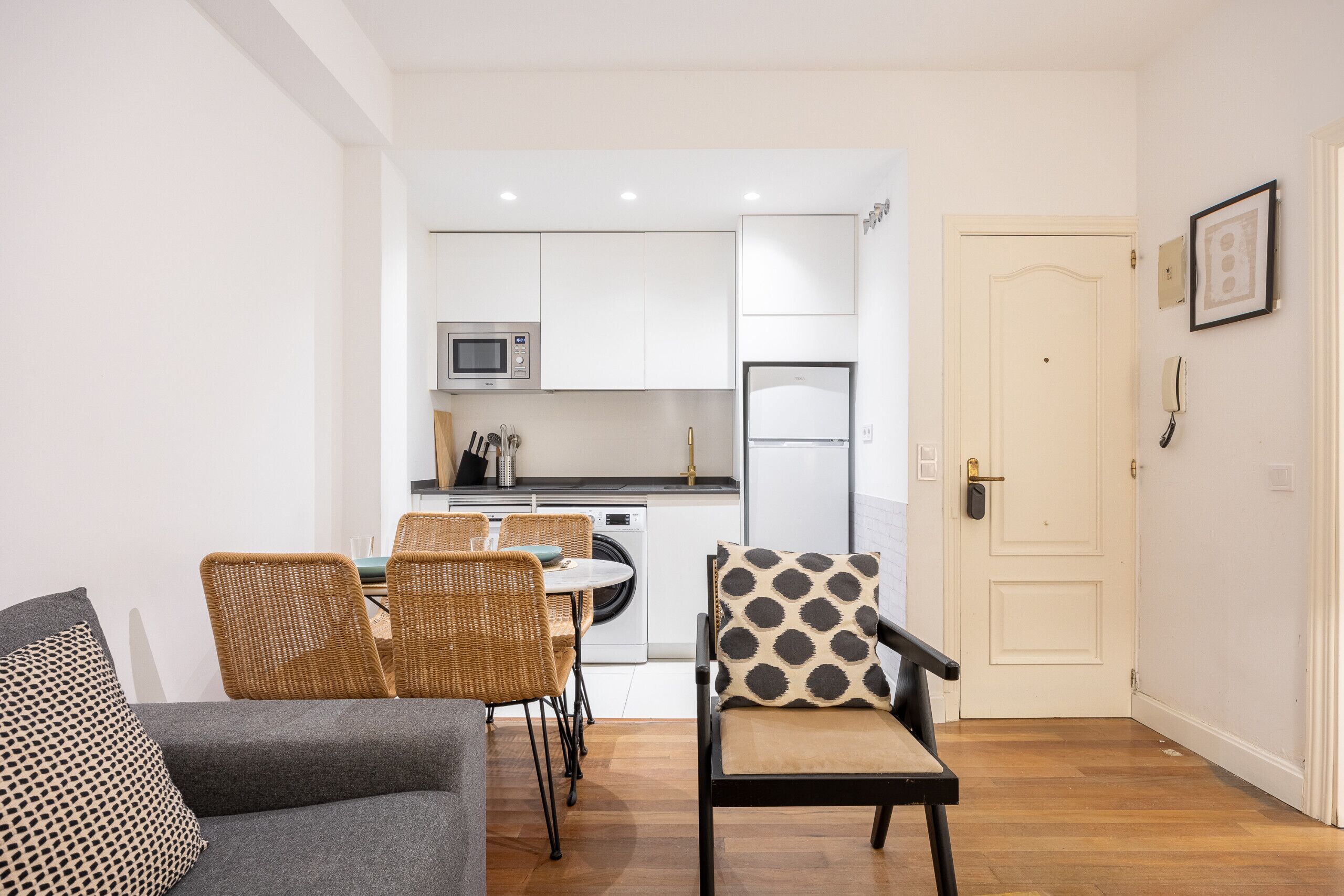 Un espacio habitable compacto con comedor, kitchenette y una puerta que da a otra habitación.