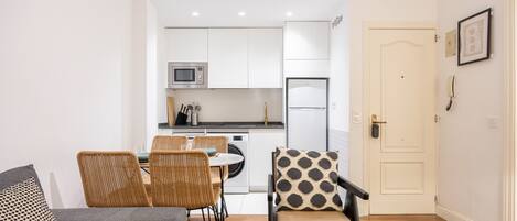 Un espacio habitable compacto con comedor, kitchenette y una puerta que da a otra habitación.