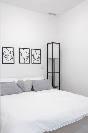 A bedroom with a bed, gray pillows, a black metal shelf, and three black line art pictures on the wall. - Stay in La Latina Stylish Apartment for Work and Study (Madrid)