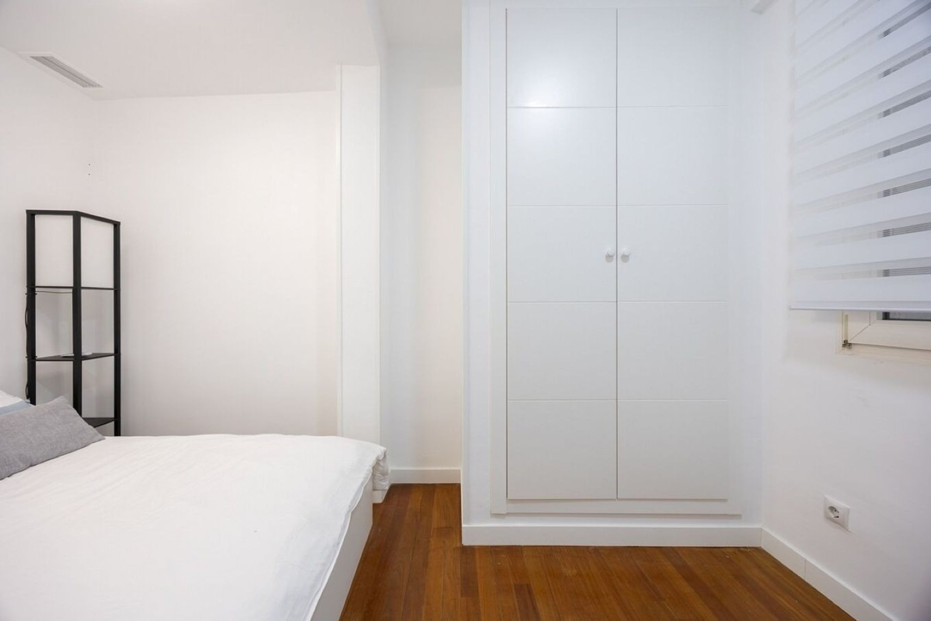 Un dormitorio con una cama, un armario y una estantería negra.