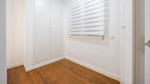 Una habitación con piso de madera, paredes blancas y un amplio armario de dos puertas.