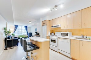 A modern kitchen with wooden cabinets, a central island, and a dining area with a black chair. - Downtown Toronto Studio Suite by the Water & FIFA (Toronto)