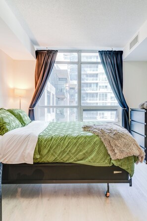 Ein Bett mit einer grünen Tagesdecke, einer flauschigen Decke und einem Fenster mit Vorhängen.