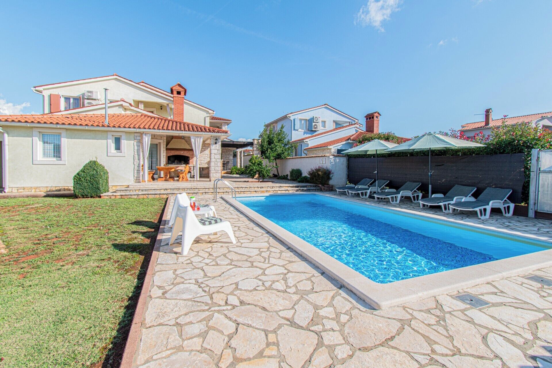 Une piscine avec des chaises longues, un espace barbecue et une terrasse en pierre.