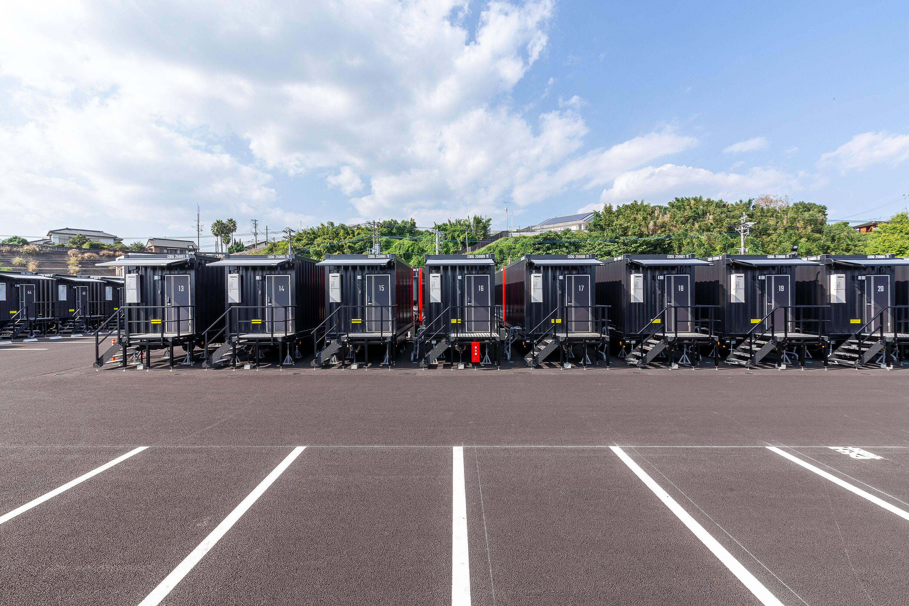 A row of portable cabins with numbers 13 to 20, arranged in a parking lot with clear markings.