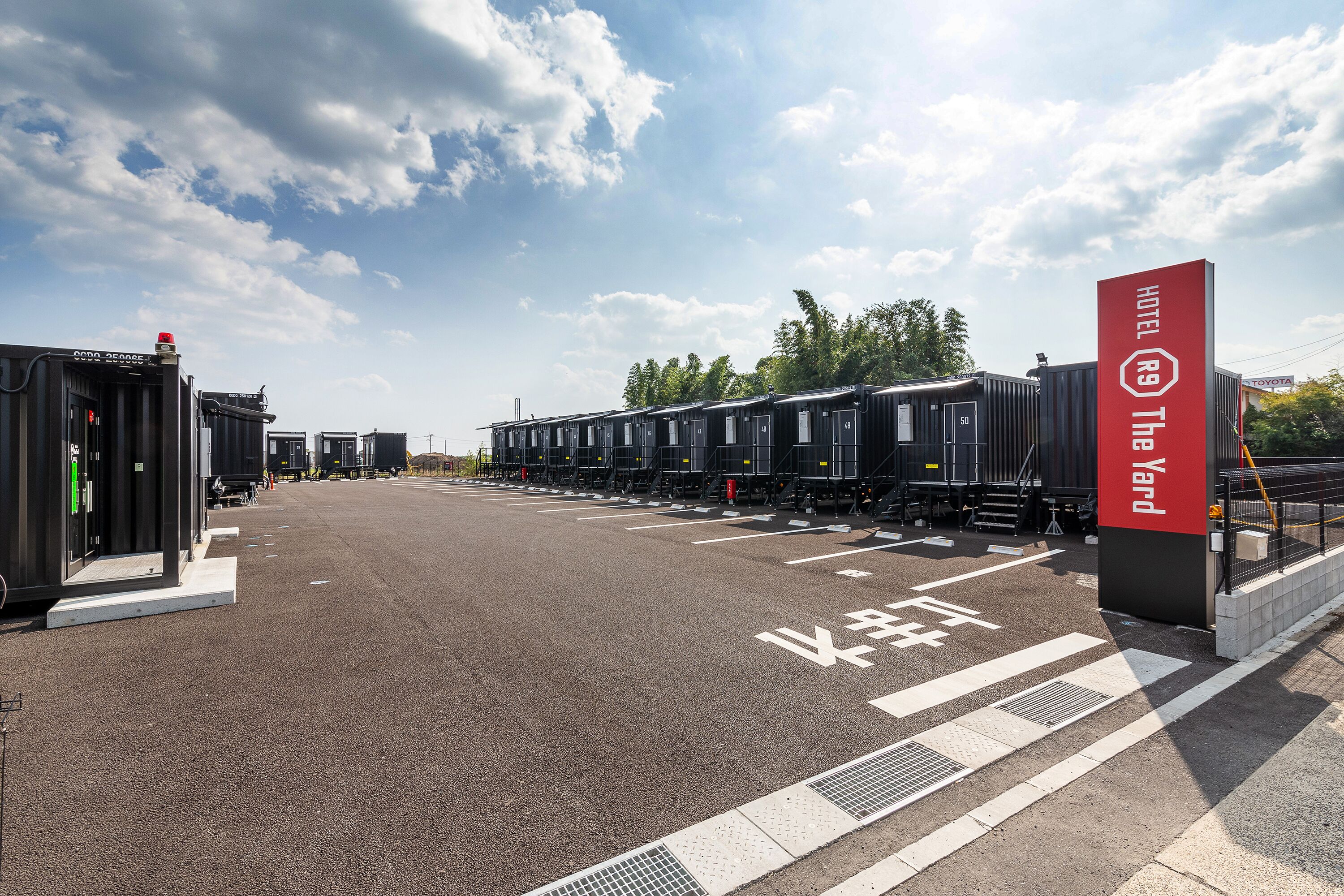 A hotel with a red sign, multiple train carriages, and a parking area.
