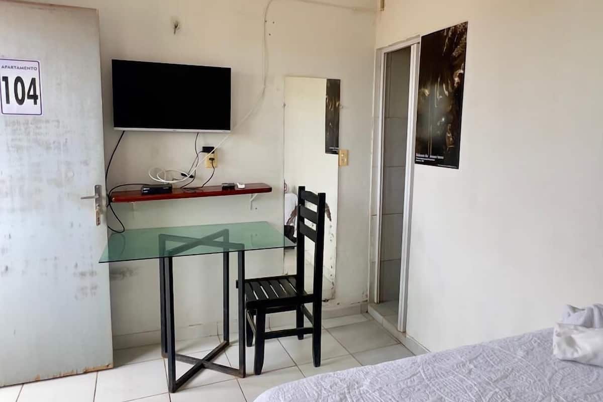 A small, sparsely furnished room with a bed, a desk with a chair, a television, and a door marked "104".