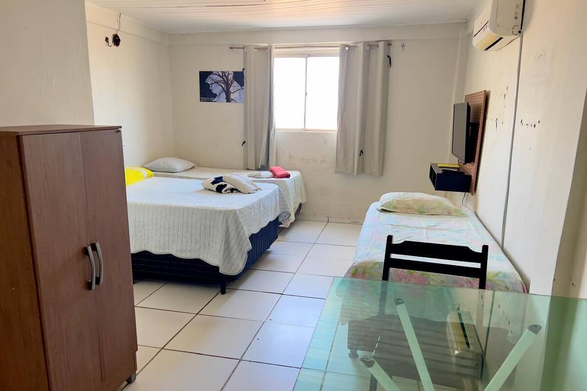 A small, well-lit room with two beds, a glass table, and a wardrobe.
