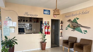 A reception area with a counter, two brown armchairs, a wall mural, and a hanging light fixture. - Pousada Rancho do Sabiá (Baraúna)