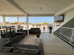 Un espacio al aire libre cubierto con sofás, una mesa de centro y un televisor montado en la pared.