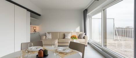 A modern living room with a dining area, large windows, and a balcony.