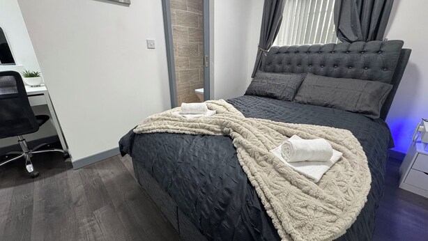 Une chambre à coucher avec un lit de couleur sombre, une couverture beige moelleuse et une tête de lit grise.
