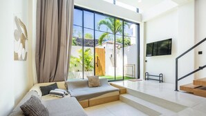 A modern living room with a sofa, a TV mounted on the wall, and a staircase leading to an upper floor.