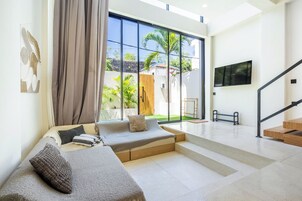 Una sala de estar moderna con un sofá, un televisor montado en la pared y una escalera que sube a un piso superior.