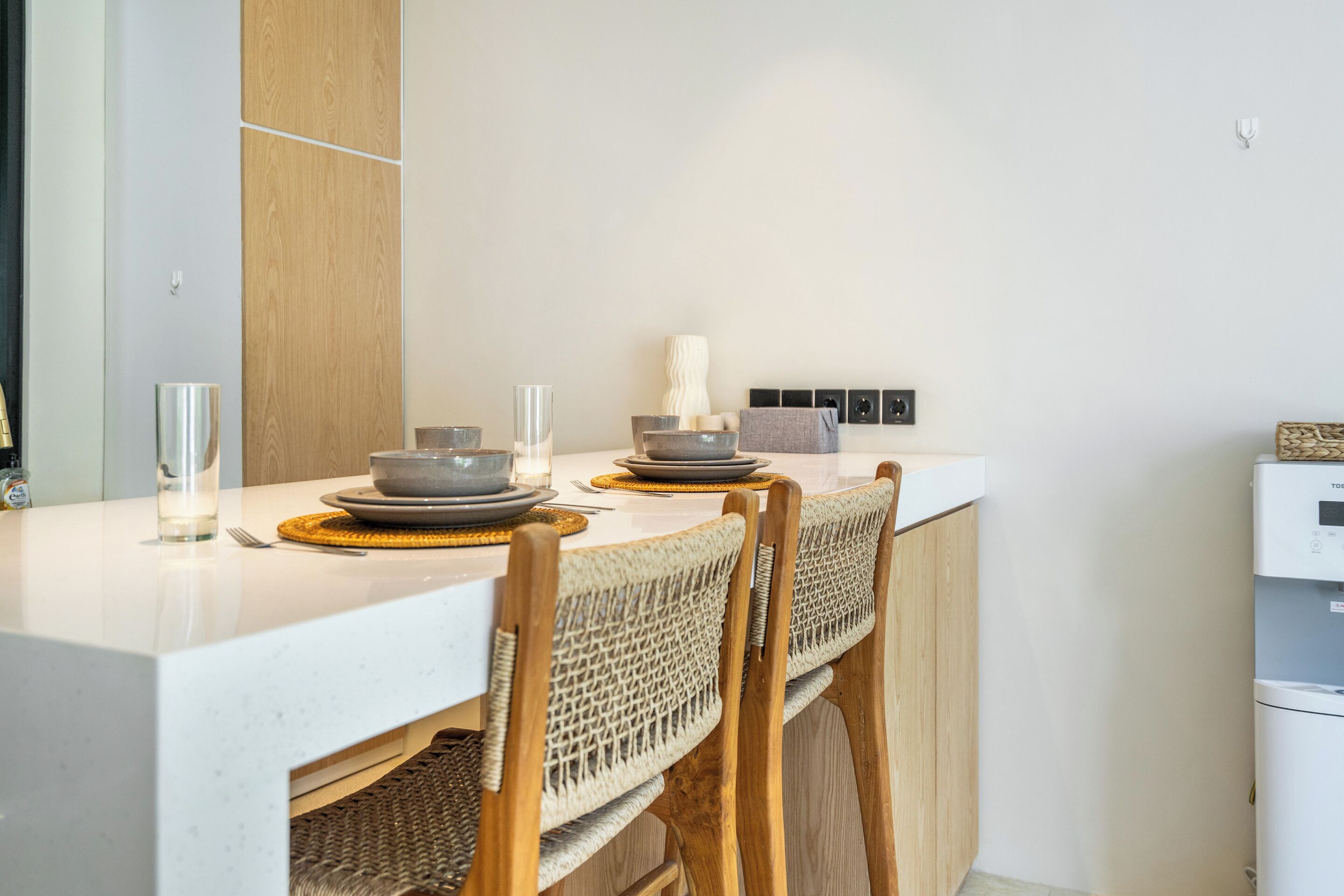 A modern kitchen with a white countertop, wooden chairs, and a built-in oven.