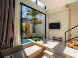 A modern living room with a large sliding glass door leading to a balcony, a flat-screen TV mounted on the wall, and a staircase with wooden steps.