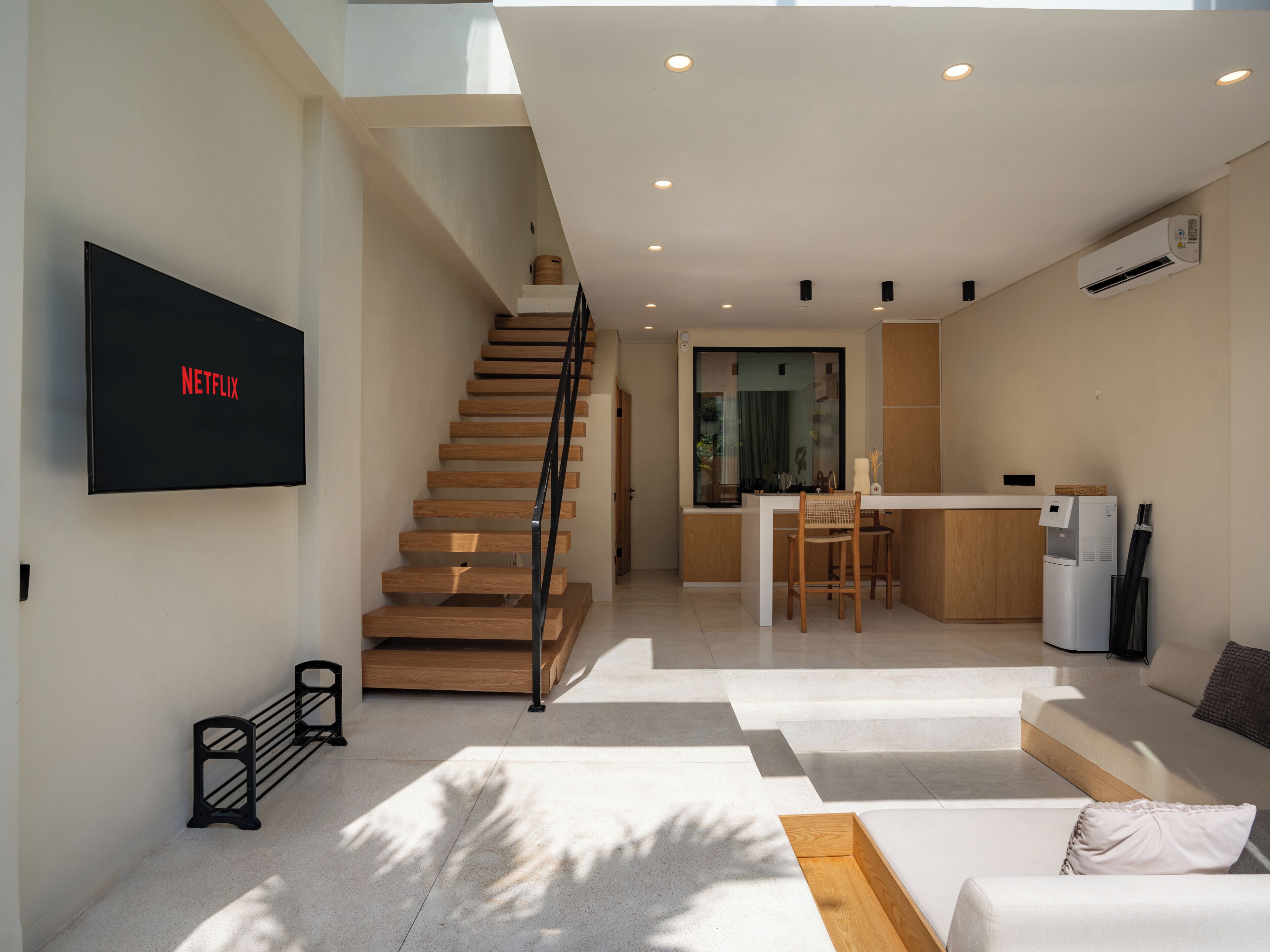 Un espace de vie moderne comprenant un escalier, un téléviseur à écran plat fixé au mur, un coin cuisine et un espace détente avec un canapé et une table basse.
