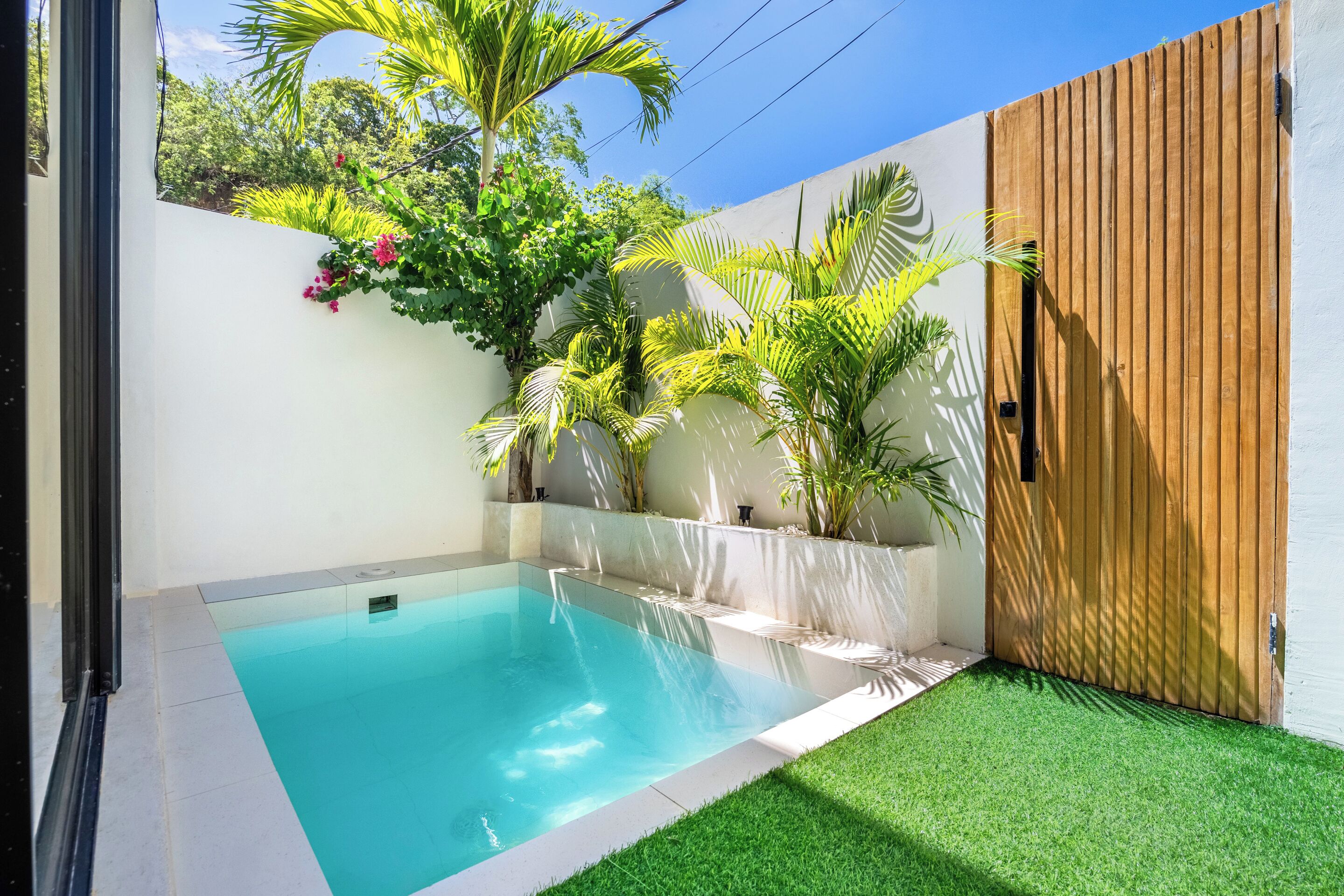 A swimming pool with a wooden fence, surrounded by green artificial grass and various plants.
