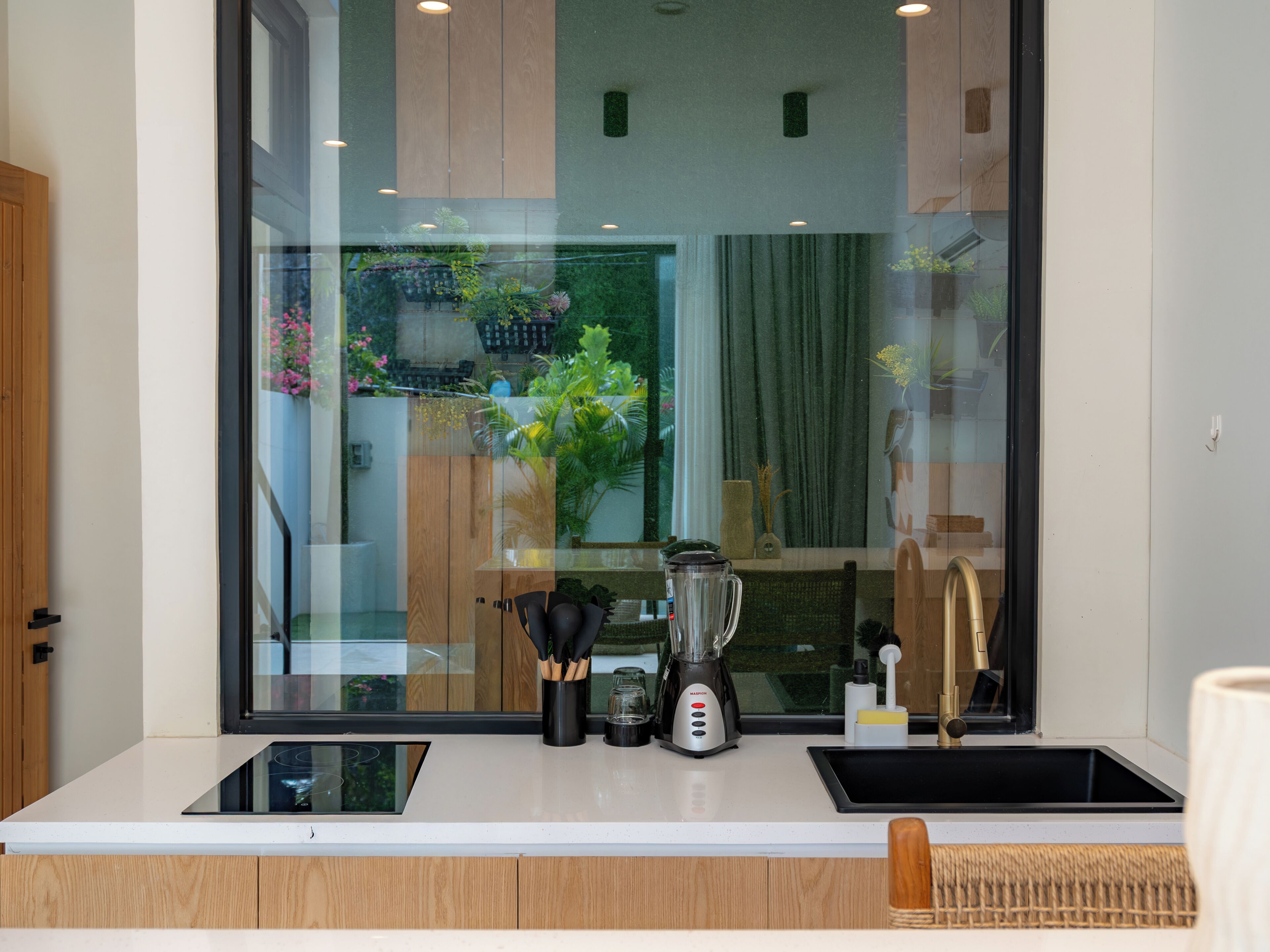 A modern kitchen with a built-in blender, a small sink, and a window overlooking a garden.