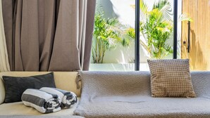 A cozy room with a sofa, a window with a view of greenery, and a wooden door.