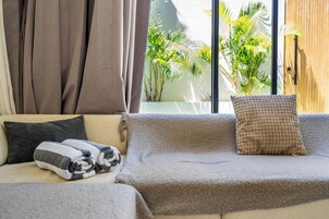 Una habitación acogedora con un sofá, un ventanal con vistas al verdor y una puerta de madera.