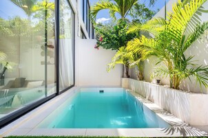 Una piscina moderna con agua azul cristalina, rodeada de abundante vegetación y paredes blancas.
