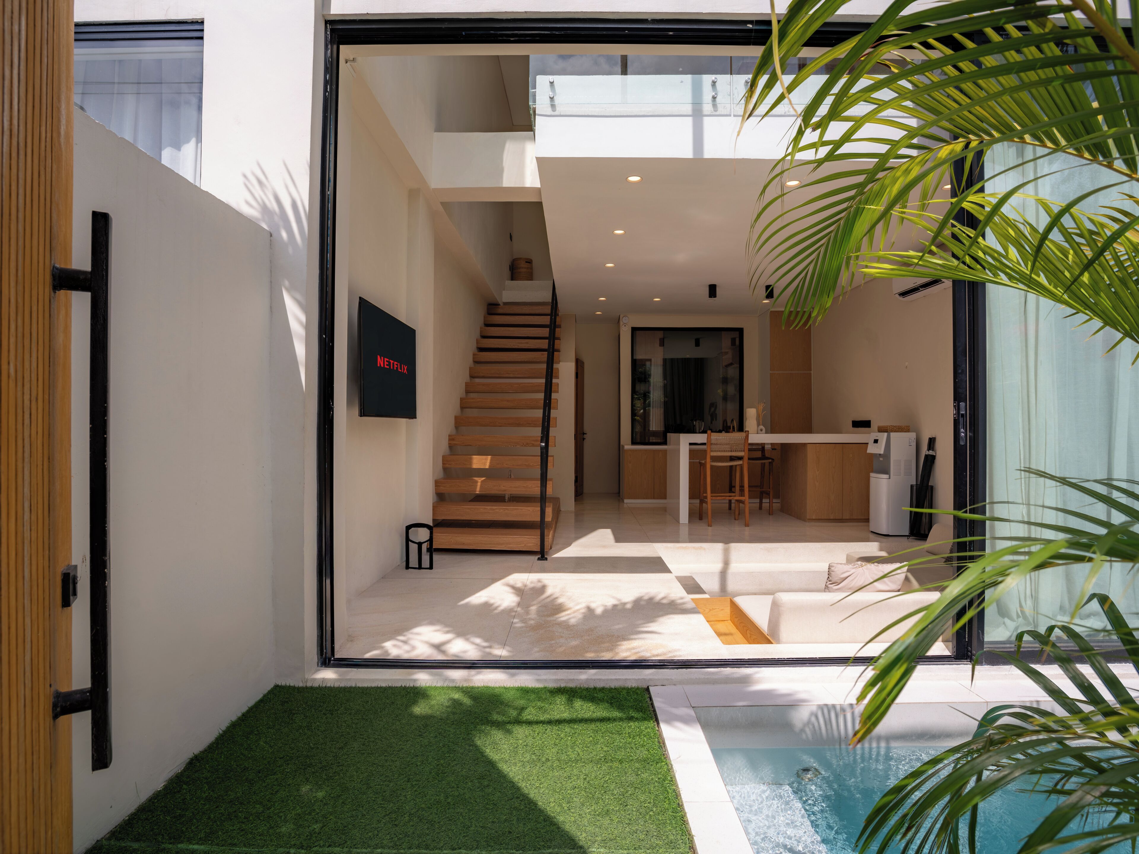 A modern interior with a staircase leading to a second floor, a kitchen area, and a small outdoor pool area.