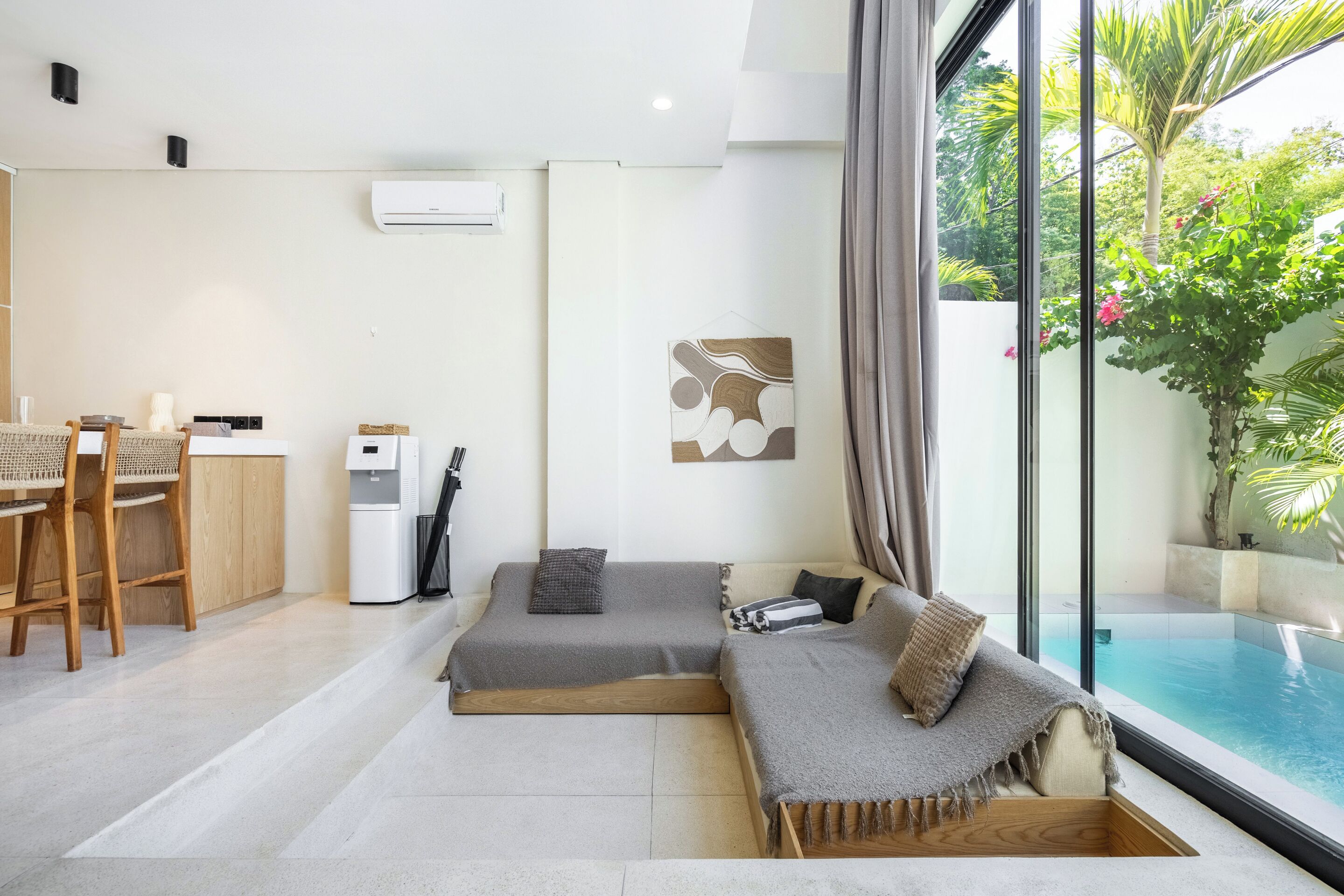 A modern living room with a sofa, a dining area with chairs, and a view of a swimming pool.