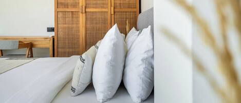 Un dormitorio con cama, almohadas, un armario de madera y una mesita de noche.