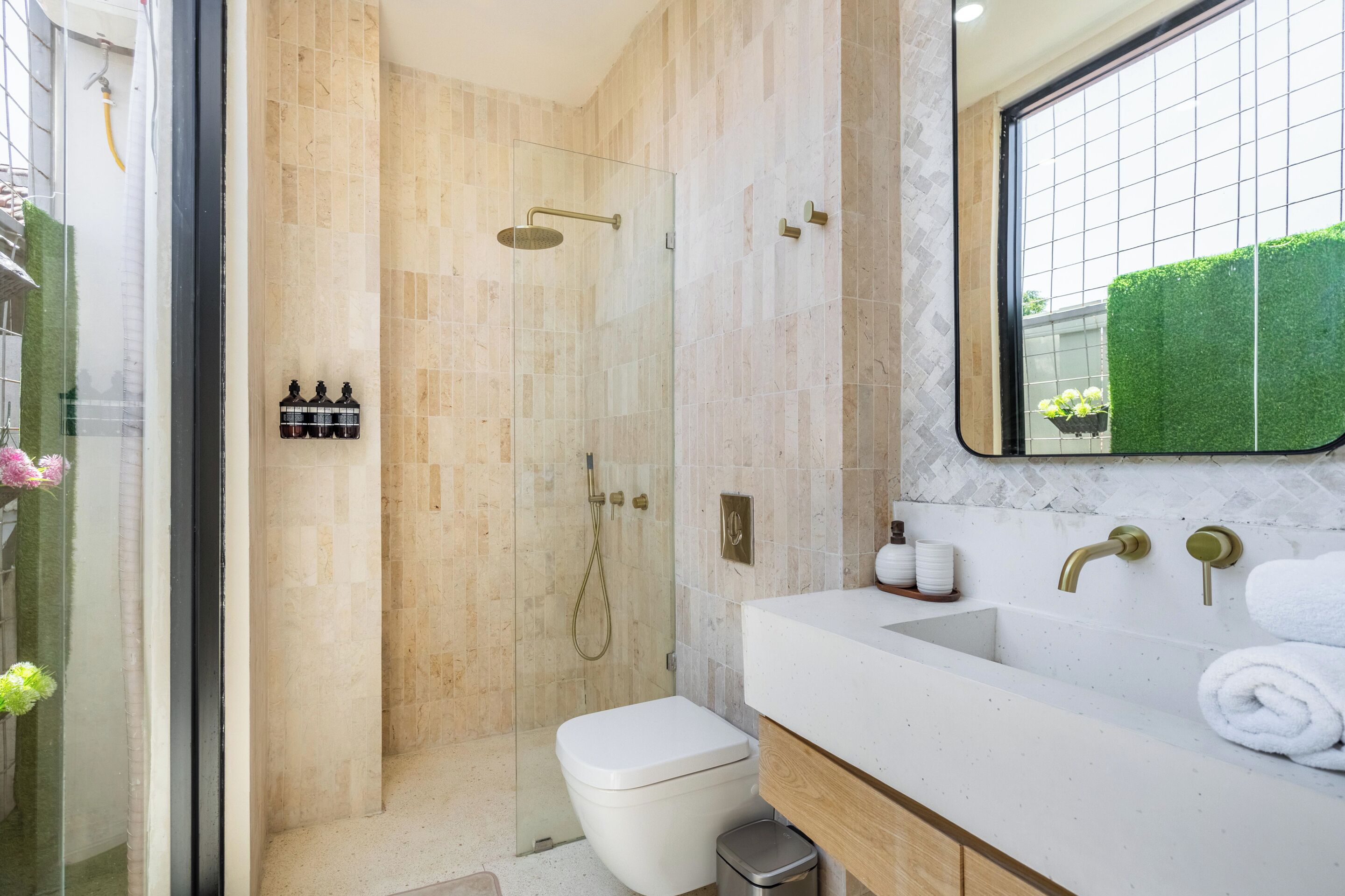 Een moderne badkamer met een douche met glazen wand, een wit toilet en een ruime wastafel met spiegel.
