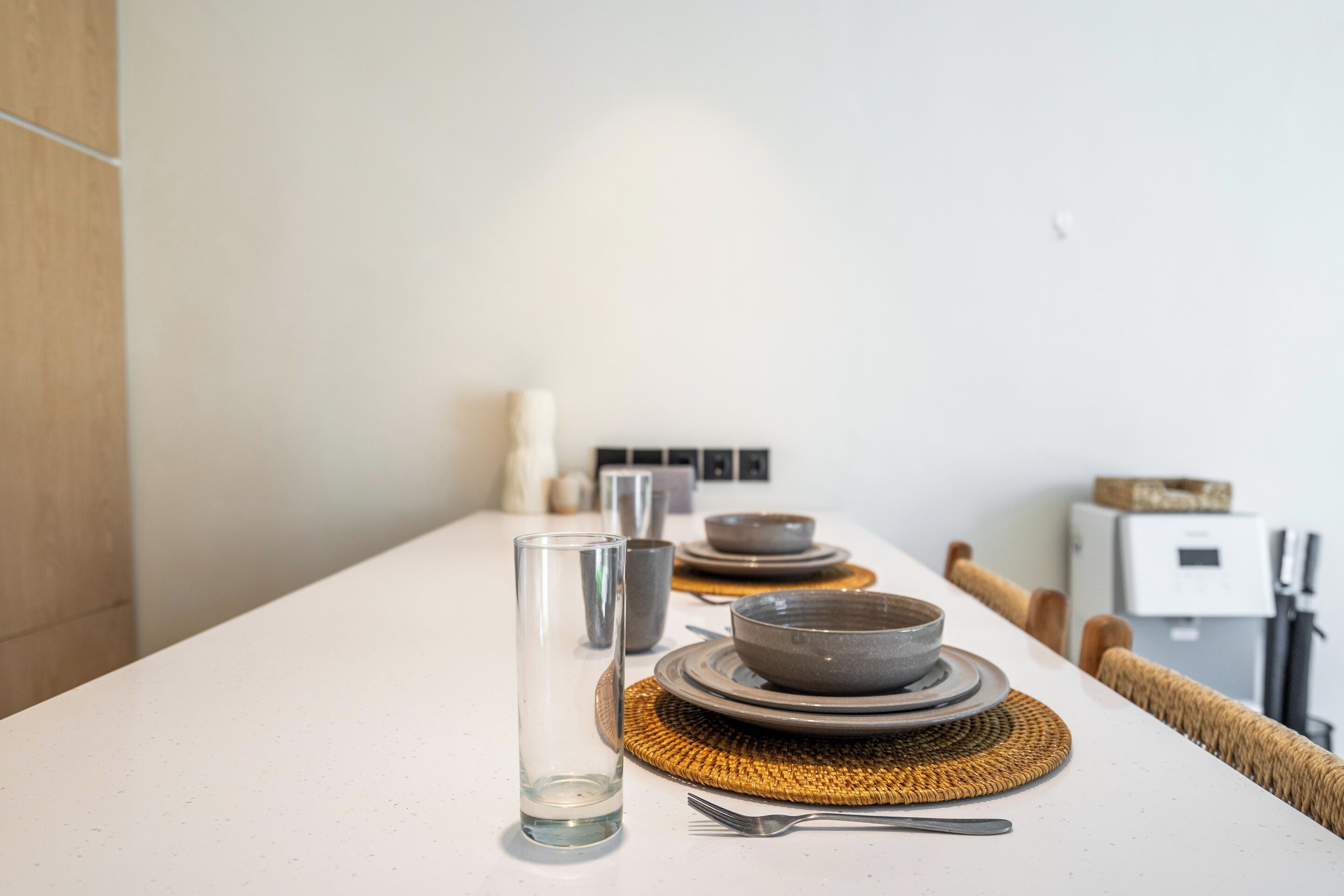 Une table à manger dressée avec des assiettes, des bols, un verre et des couverts, agrémentée d’un set de table en fibres tressées et d’une chaise.