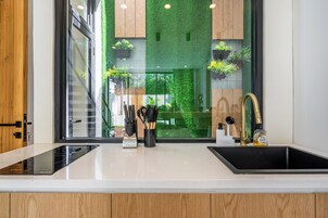 Una cocina moderna con encimera blanco y negro, estufa integrada y un lavamanos con grifo dorado. Hay plantas en macetas en el alféizar de la ventana y un juego de utensilios de cocina sobre la encimera.