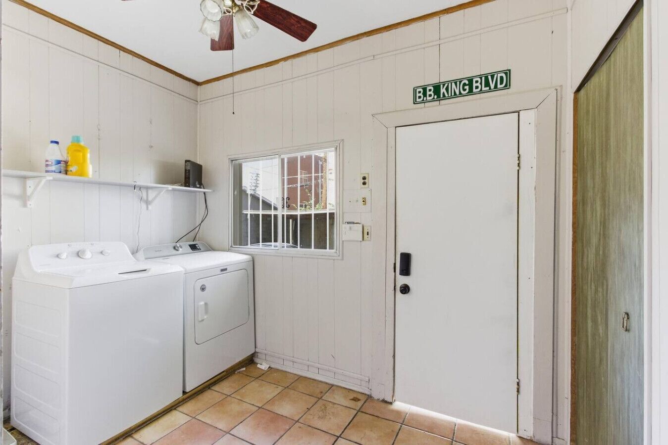 A laundry room with a washing machine, dryer, and a window. There is a door with a sign above it reading "B.B. KING BLVD."