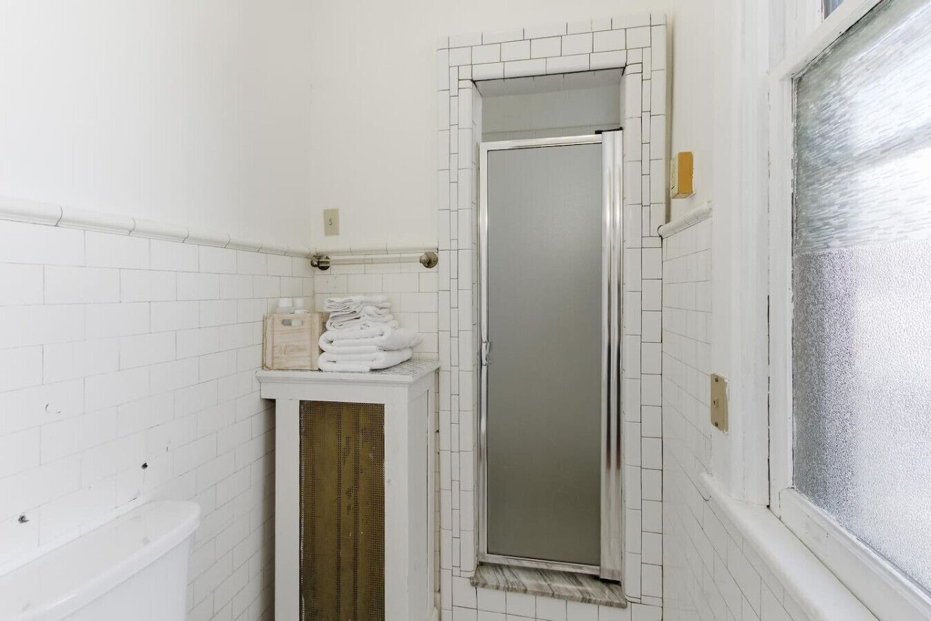 A narrow bathroom with white tiled walls, a white bathtub, and a tall mirror.