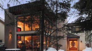 Ein modernes, zweistöckiges Gebäude mit Glasfassade, einer verschneiten Terrasse mit Sitzgelegenheiten und einem gut beleuchteten Eingang.