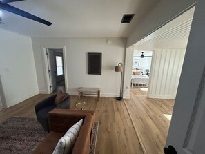 Een ruime woonkamer met houten vloeren, een bruine bank, een houten bankje en een vloerlamp.