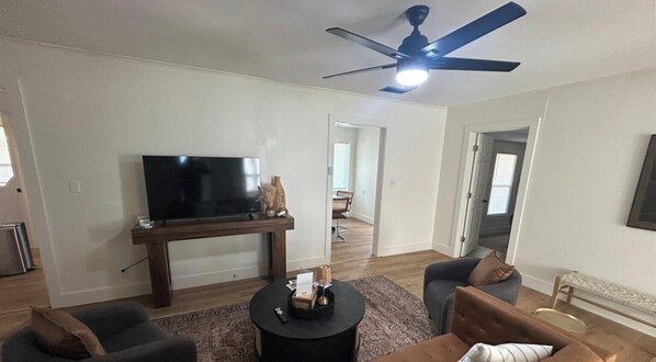 Una sala de estar con televisión de pantalla plana, ventilador de techo, mesa de centro y sofá.