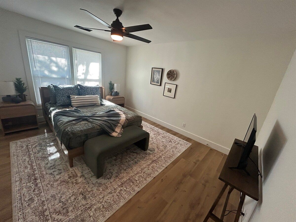 A bedroom with a bed, bedside tables, a desk, a ceiling fan, and a TV.