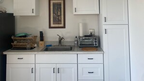 Een kleine keuken met witte kastjes, een spoelbak, een broodrooster en een klein aanrecht.