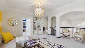 A spacious living room with a white sofa, a coffee table with board games, a globe chandelier, and a staircase leading to an upper level. - Spacious 6BR Villa for 14 · Home Theater, Game Loft & Gym · 10 Min to Universal (McKinney)