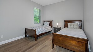 Ein Schlafzimmer mit zwei hölzernen Betten, einem Nachttisch, einem Fenster mit Jalousien und einem Deckenventilator.