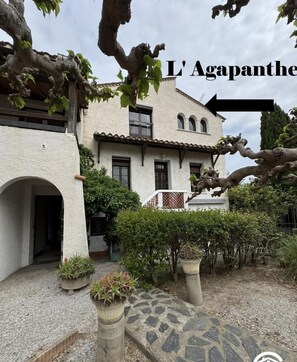 A two-story building with a white facade, a balcony, and a stone pathway leading to the entrance. - L' Agapanthe - SAINTE MARIE LA MER (SAINTE MARIE LA MER)