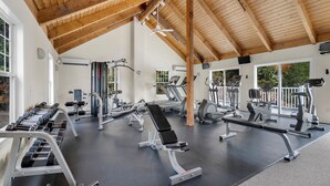 Une salle de sport équipée de divers appareils d’exercice, avec des poutres en bois au plafond et de grandes fenêtres.