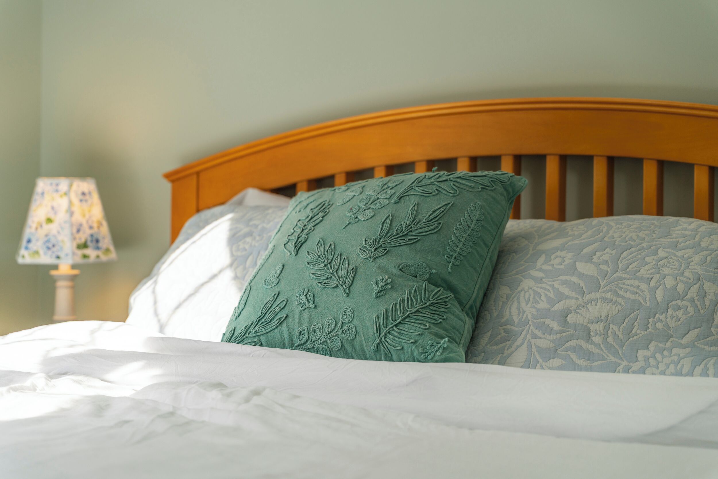 A bed with a wooden headboard, a green pillow with leaf patterns, and a white pillow with a floral design.