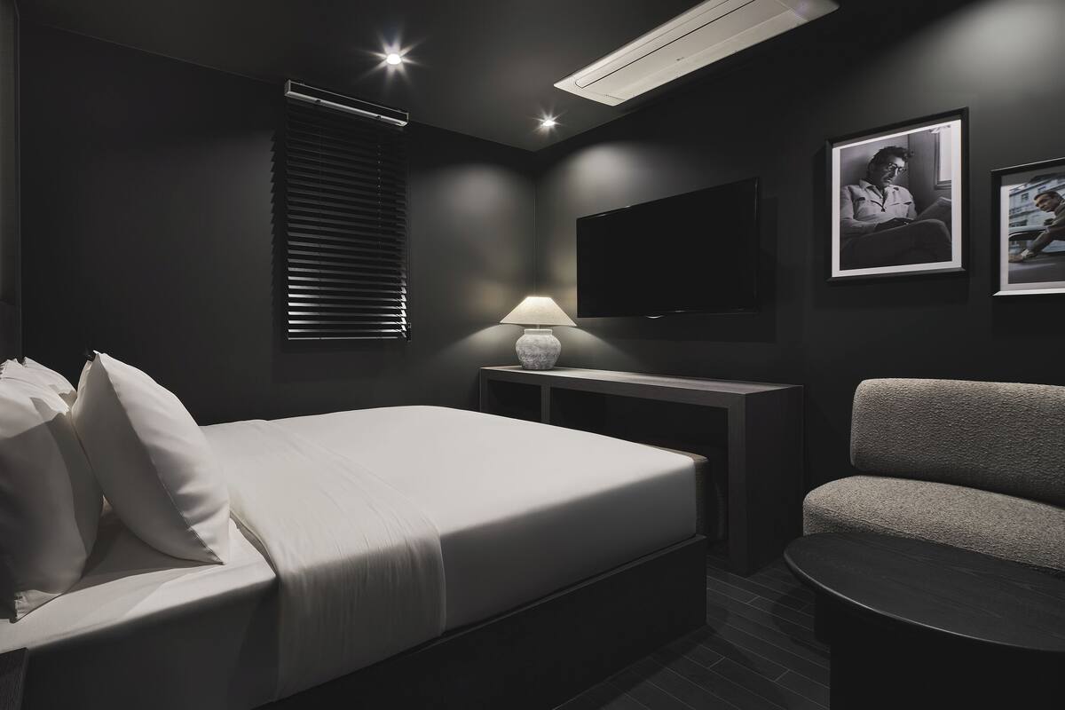 A modern hotel room with a bed, a desk, a chair, and a TV.