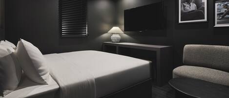 A modern hotel room with a bed, a desk, a chair, and a TV.