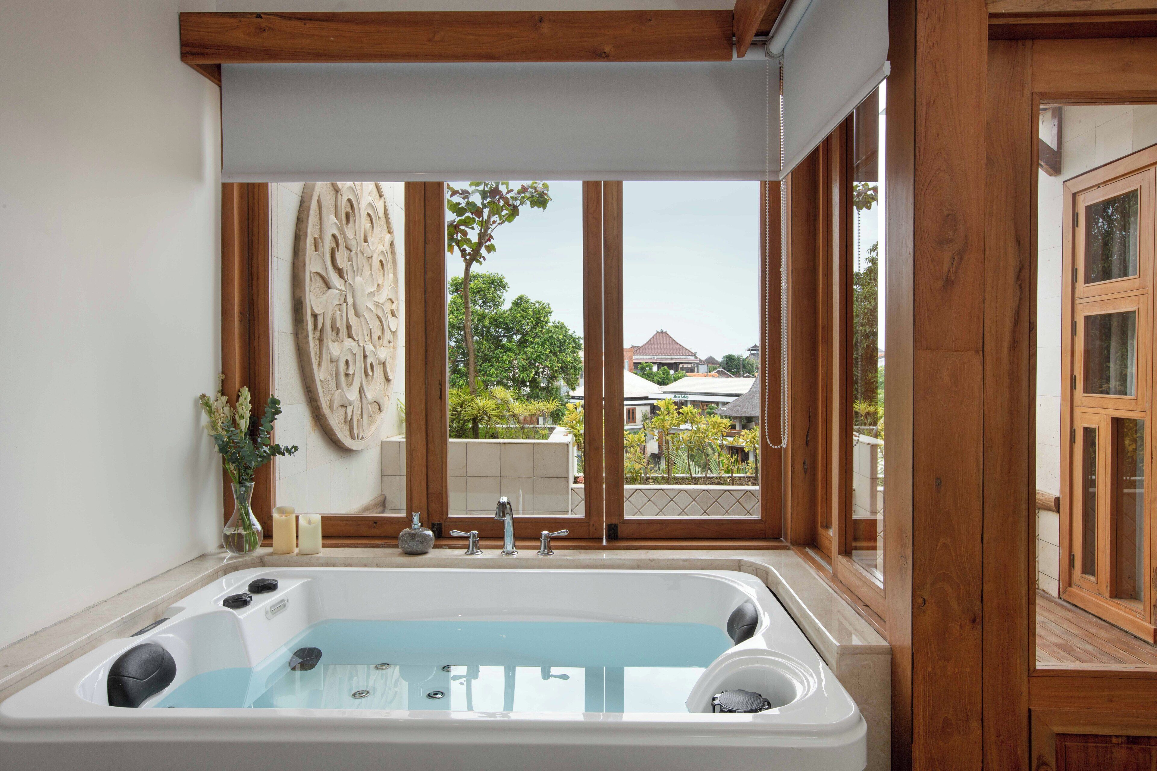 A bathroom with a large bathtub, wooden window frames, and a view of a house.