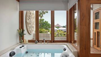 A bathroom with a large bathtub, wooden window frames, and a view of a house.