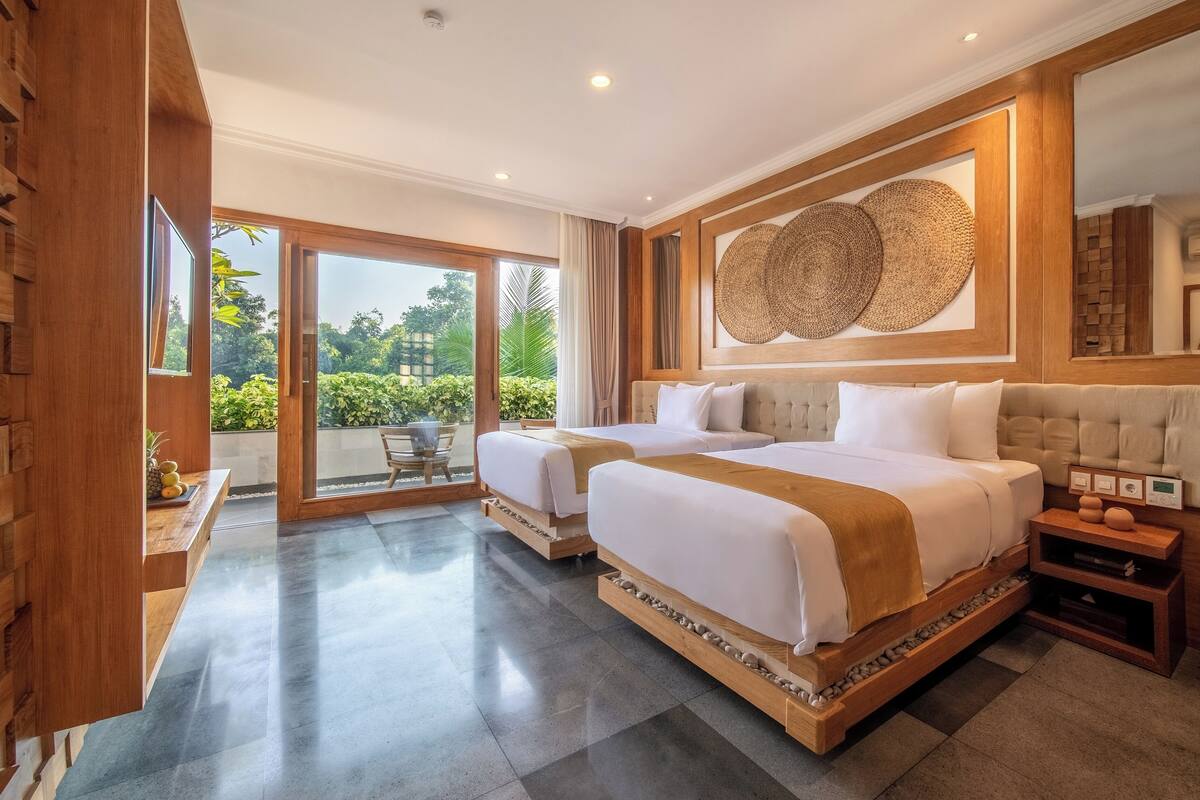 A hotel room with two beds, a large window, and a view of greenery.